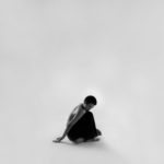 man in black and white hoodie sitting on white surface